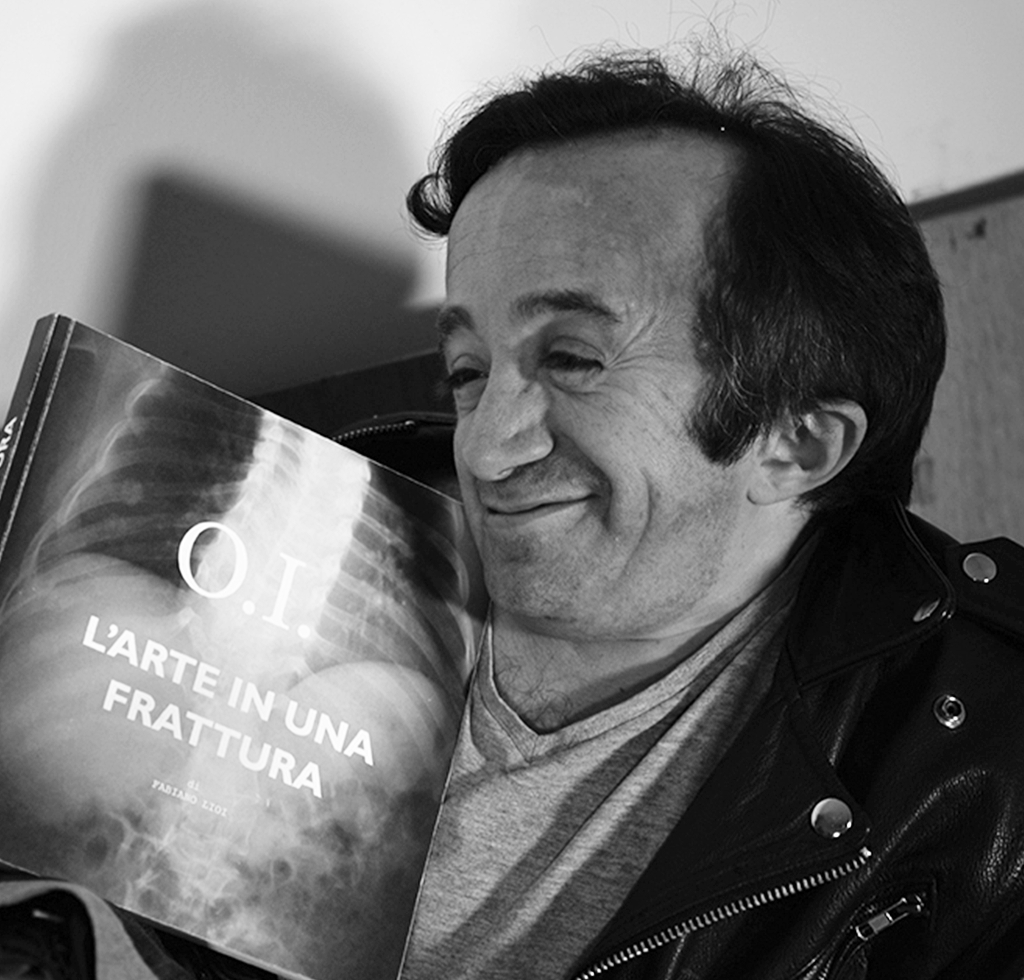 Fabiano Lioi Sorride con il suo libro O.I. L'arte in una frattura in mano, quasi sdraiato sulla sedia, e ti invita a leggere gli articoli del Blog!